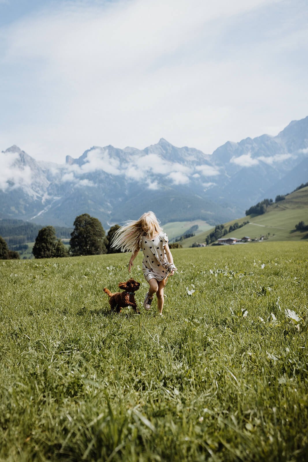 kind spielt in der wiese mit hund vor den bergen der hochkönig region